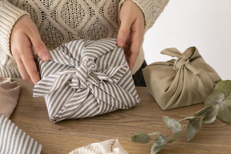 Manos mostrando una de las ideas creativas para envolver regalos usando recortes de telas o pañuelos.