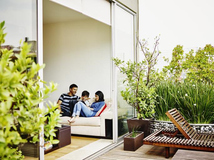 Papá, mamá e hijo sentados en el mueble de su apartamento con zona verde en el patio.