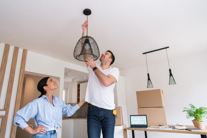 Hombre poniendo lámpara en la sala con su esposa para decorar un apartamento pequeño.