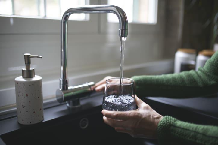 Mujer abriendo grifo para llenar un vaso a modo de referencia para ahorrar en el hogar.