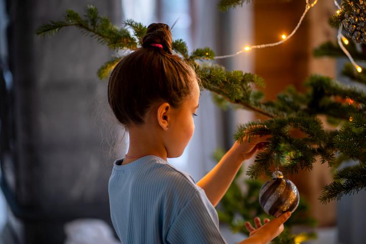 Niña poniendo una bola al árbol de Navidad siguiendo las tendencias de decoración navideña.