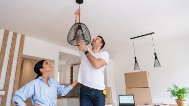 Hombre poniendo lámpara en la sala con su esposa para decorar un apartamento pequeño.