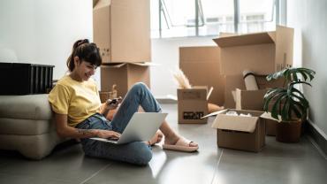 Imagen de referencia para multifamily en Bogotá, una mujer joven sentada en la sala de su nuevo apartaestudio mientras desempaca.